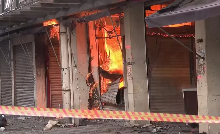 Incêndio de Grandes Proporções Atinge Shopping 25 de Março no Brás, em São Paulo Na manhã desta quarta-feira (30), um incêndio de grandes proporções atingiu o Shopping 25 de Março, localizado na Rua Barão de Ladário, no Brás, região central de São Paulo. O fogo teve início por volta das 6h40, e ainda não se sabe o que causou o incidente. Pelo menos 22 viaturas e 65 bombeiros foram mobilizados para combater as chamas, que rapidamente se Às 8h, parte do teto do shopping desabou, gerando uma coluna de fumaça densa de mais de 150 metros, visível de diversas partes da cidade. A área afetada, com cerca de 18 mil metros quadrados, abriga um comércio popular com grande quantidade de material combustível, o que contribui para a rápida propagação do fogo. O Auto de Vistoria do Corpo de Bombeiros (AVCB) do shopping foi vencido desde agosto, mas o estabelecimento continuou funcionando enquanto passava pelo processo de regularização Para garantir a segurança e facilitar o trabalho das equipes de emergência, a Polícia Militar interditou algumas vias, e pelo menos sete linhas de ônibus foram desviadas. A Companhia de Engenharia de Tráfego (CET) recomenda que os motoristas evitem uma região, onde vários segmentos estratégicos estão bloqueados. O governo estadual informou que a Sabesp forneceu água adequada e o bom funcionamento dos hidrantes no local, descartando problemas de abastecimento. Uma jovem de 21 anos, que inalou fumaça, foi levada ao Hospital do Tatuapé e está em estado estável. Este é o segundo incêndio registrado na região do Brás nesta semana. No último domingo (27), outro galpão comercial na Rua Doutor João Alves de Lima foi destruído por um incêndio, destacando a vulnerabilidade dos centros comerciais da área.