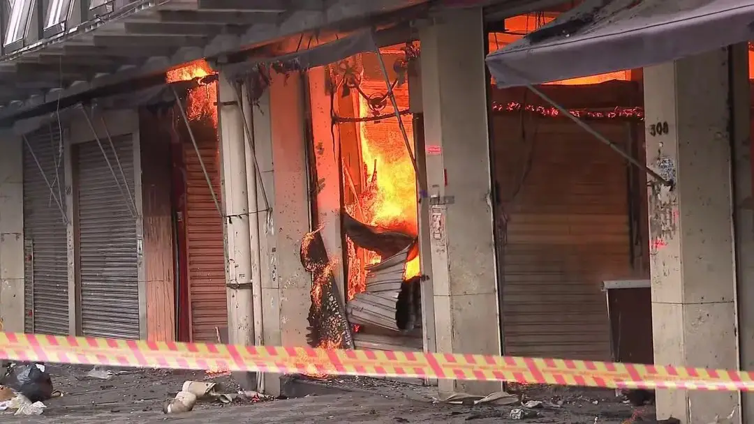 Incêndio de Grandes Proporções Atinge Shopping 25 de Março no Brás, em São Paulo Na manhã desta quarta-feira (30), um incêndio de grandes proporções atingiu o Shopping 25 de Março, localizado na Rua Barão de Ladário, no Brás, região central de São Paulo. O fogo teve início por volta das 6h40, e ainda não se sabe o que causou o incidente. Pelo menos 22 viaturas e 65 bombeiros foram mobilizados para combater as chamas, que rapidamente se Às 8h, parte do teto do shopping desabou, gerando uma coluna de fumaça densa de mais de 150 metros, visível de diversas partes da cidade. A área afetada, com cerca de 18 mil metros quadrados, abriga um comércio popular com grande quantidade de material combustível, o que contribui para a rápida propagação do fogo. O Auto de Vistoria do Corpo de Bombeiros (AVCB) do shopping foi vencido desde agosto, mas o estabelecimento continuou funcionando enquanto passava pelo processo de regularização Para garantir a segurança e facilitar o trabalho das equipes de emergência, a Polícia Militar interditou algumas vias, e pelo menos sete linhas de ônibus foram desviadas. A Companhia de Engenharia de Tráfego (CET) recomenda que os motoristas evitem uma região, onde vários segmentos estratégicos estão bloqueados. O governo estadual informou que a Sabesp forneceu água adequada e o bom funcionamento dos hidrantes no local, descartando problemas de abastecimento. Uma jovem de 21 anos, que inalou fumaça, foi levada ao Hospital do Tatuapé e está em estado estável. Este é o segundo incêndio registrado na região do Brás nesta semana. No último domingo (27), outro galpão comercial na Rua Doutor João Alves de Lima foi destruído por um incêndio, destacando a vulnerabilidade dos centros comerciais da área.